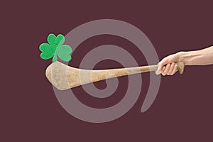 Man hands holdÂ hurly sticks â€“ hurleys. Green clover balancing on top of it against a green background. Ireland traditional
